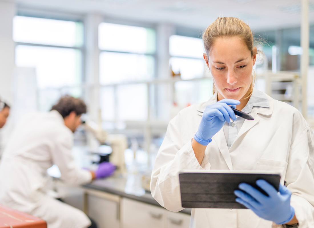 Female scientist wearing a lab coat and nitrile gloves is working with a digital tablet and stylus in the laboratory.