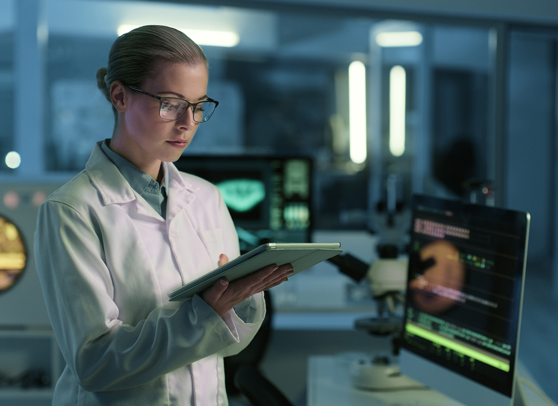 A female laboratory professional looks at a tablet while standing in a darkened laboratory, illustrating the review of laboratory enforcement actions.