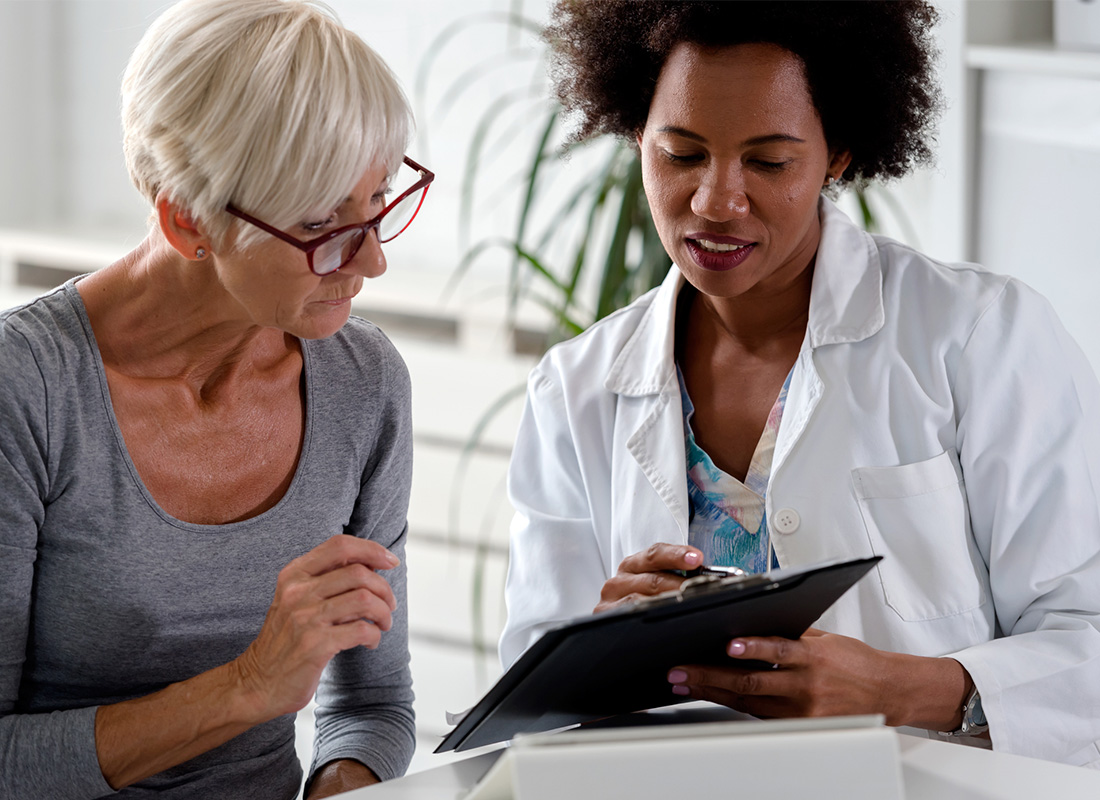 An older female patient discusses test results with her female doctor, who is holding a clipboard.