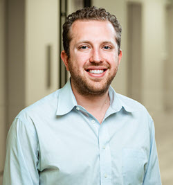 A headshot of Nathan Buchbinder, a fair-skinned man with light brown hair wearing a pale blue button-down shirt.