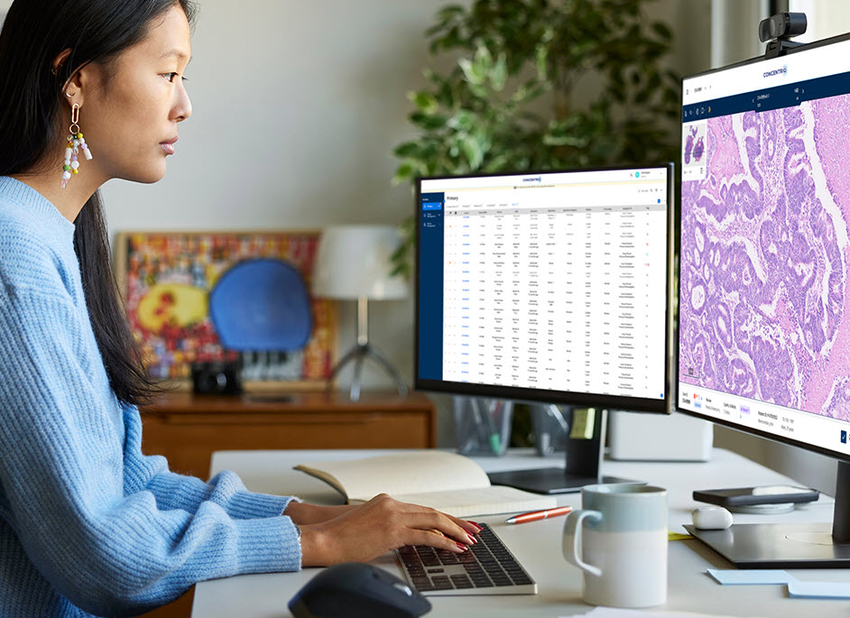 A female pathologist examines whole-slide images and digital pathology data on two computer monitors.