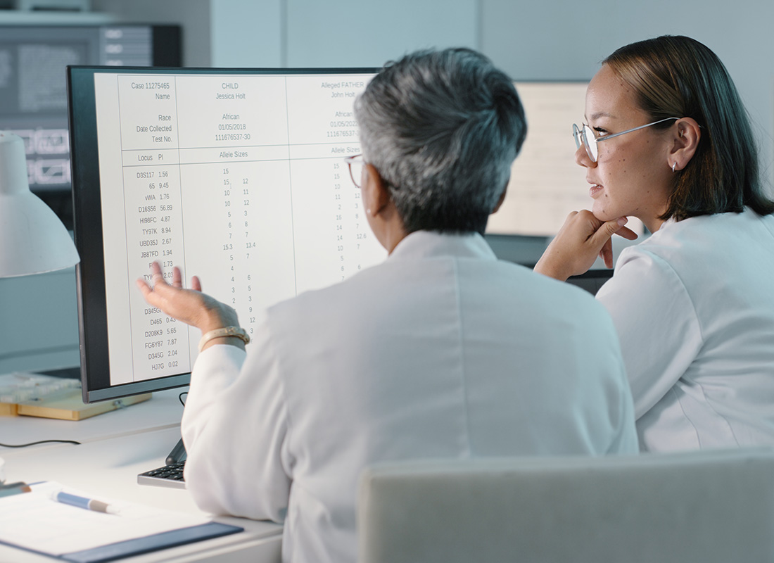 Two female healthcare professionals sit at a desk and discuss information on a computer screen.