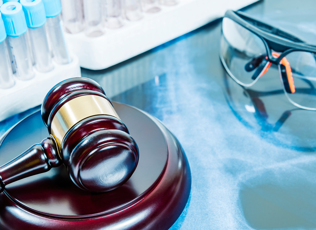 A judge’s gavel sits on a lab bench next to racks of test tubes and a pair of safety glasses, illustrating legal issues related to laboratories.