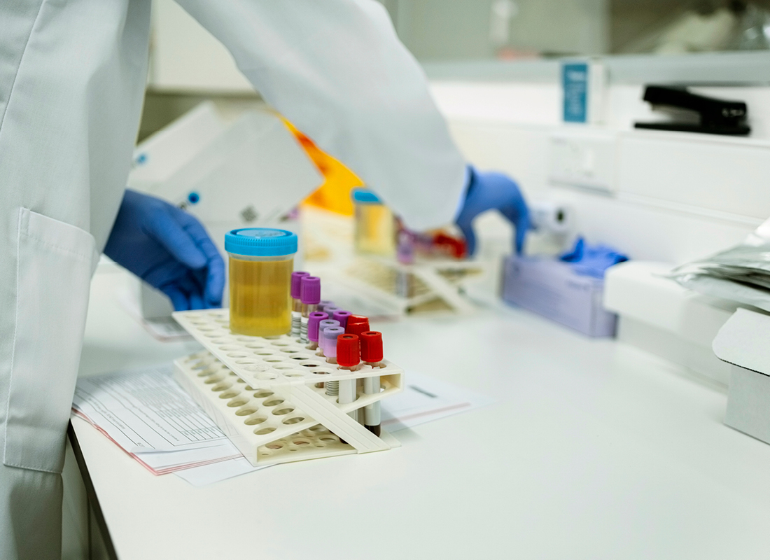 Cropped shot of a lab technician working with blood and urine samples on a test tube rack in a pathology laboratory, illustrating the concept of fraud involving urine drug testing.