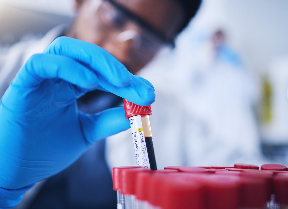 A laboratory professional removes a test tube of blood from a rack on a lab bench, illustrating the concept of lab tests involving blood.