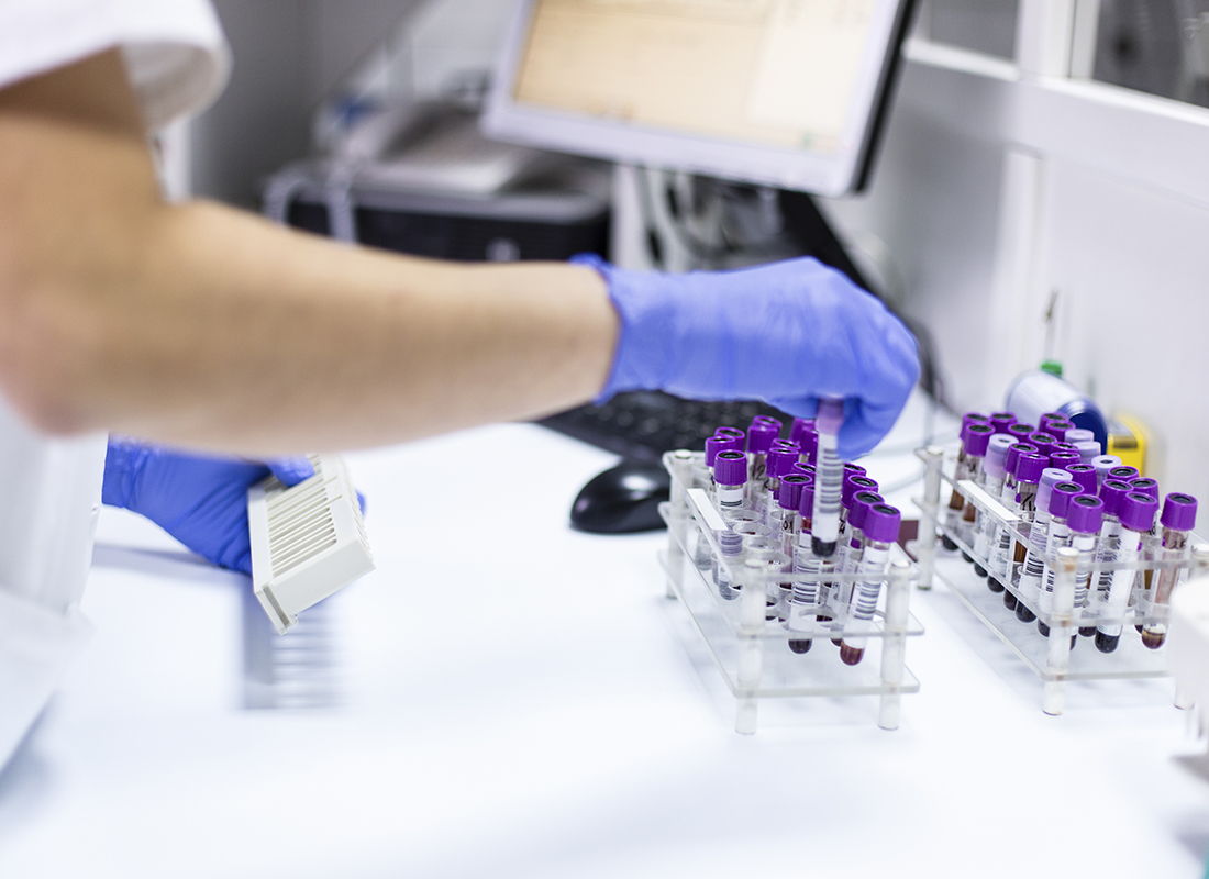 A closeup of a laboratorian removing a tube of blood from a rack on a laboratory bench.