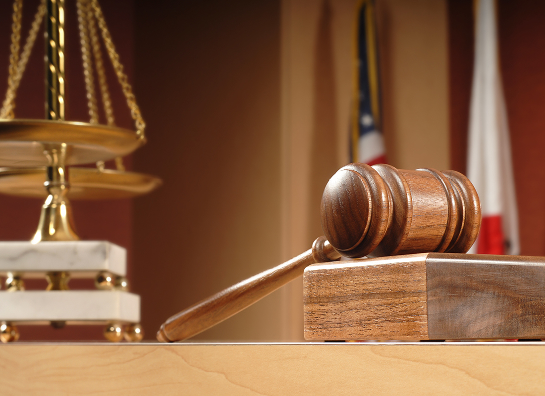 A closeup of a scale and judge’s gavel sitting on a desk in a courtroom, illustrating a legal concept.